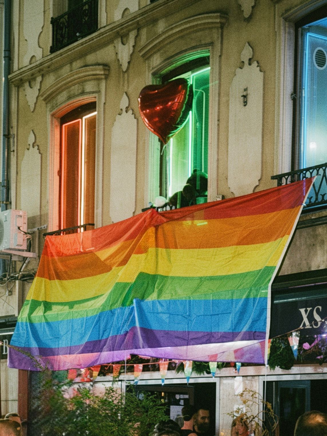 Drapeau arc-en-ciel devant la façade du XS BAR, bar gay à Lyon, éclairée de néons un soir de fête